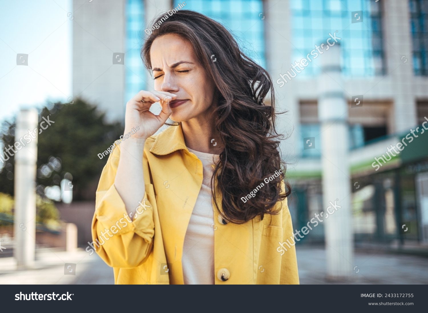 Woman with allergy symptom blowing nose. Outdoor shot of displeased Caucasian woman feels allergy, holds white tissuue, stands near tree with blossom, feels unwell, sneezes all time. Spring time. #2433172755