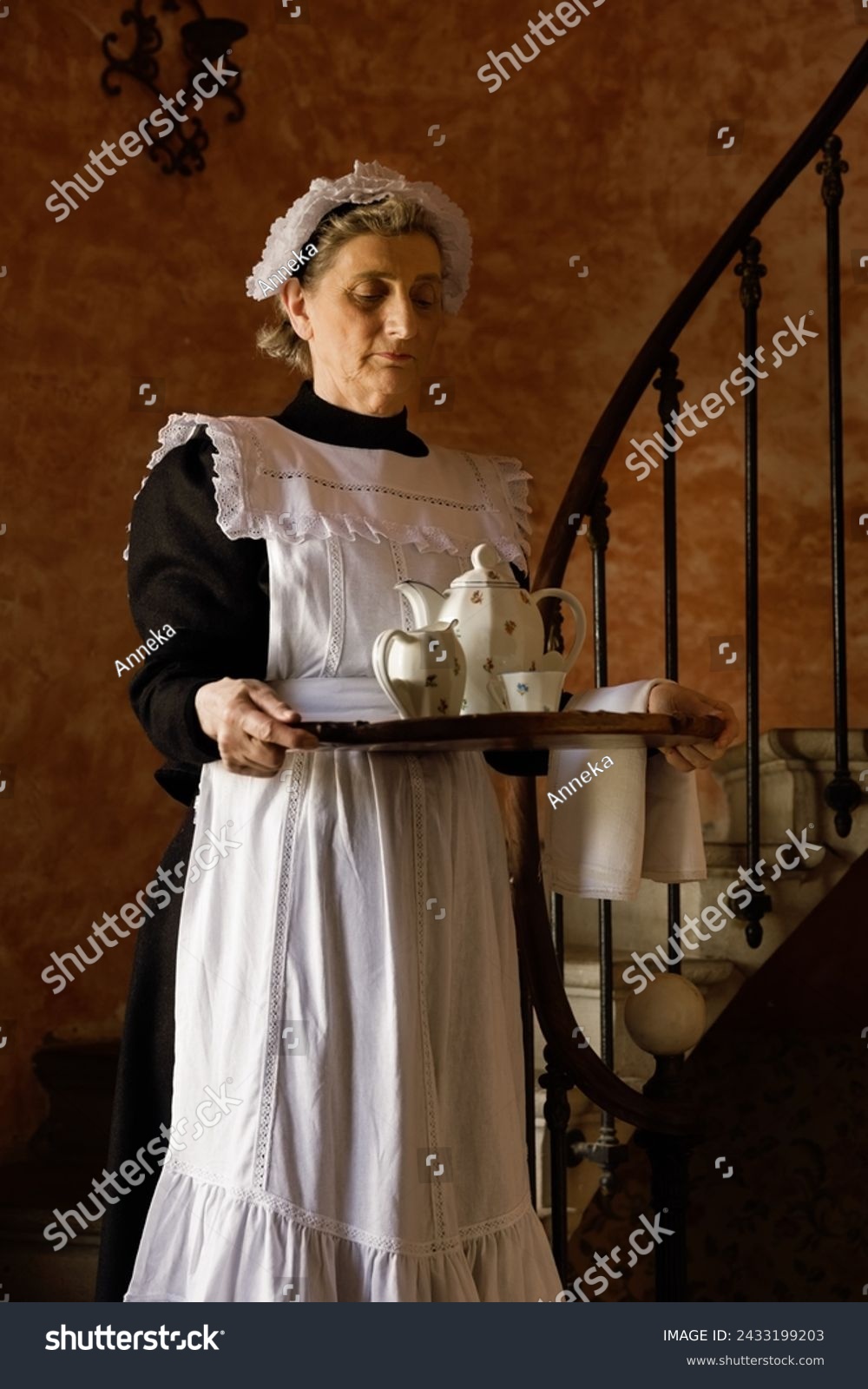 Victorian maid or servant in black dress, lace cap and white apron working in a 19th century interior #2433199203