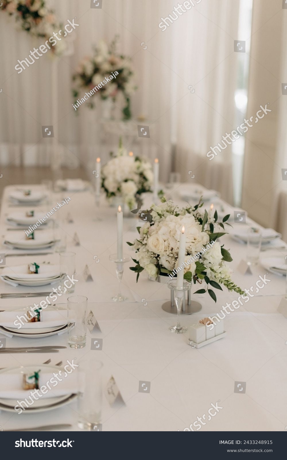 Many small white flower arrangements with roses, eustoma and various flowers in clear glass vases. On the festive table in the wedding banquet area, compositions of flowers and greenery, candles are p #2433248915