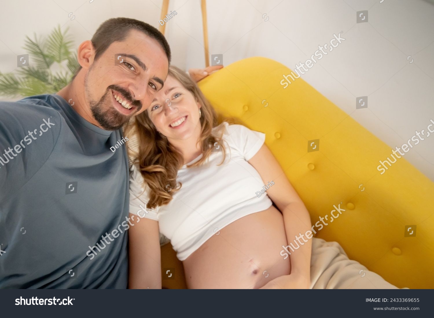 A pregnant woman and her husband are photographing themselves on the cell phone at home. High quality photo #2433369655