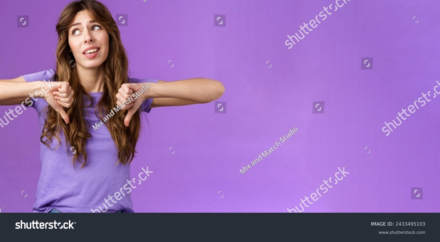 Unimpressed ignorant snobbish attractive curly-haired girl disagree lame idea look away disappointed show thumbs down dislike disapproval gesture not interested upset purple background. #2433495103