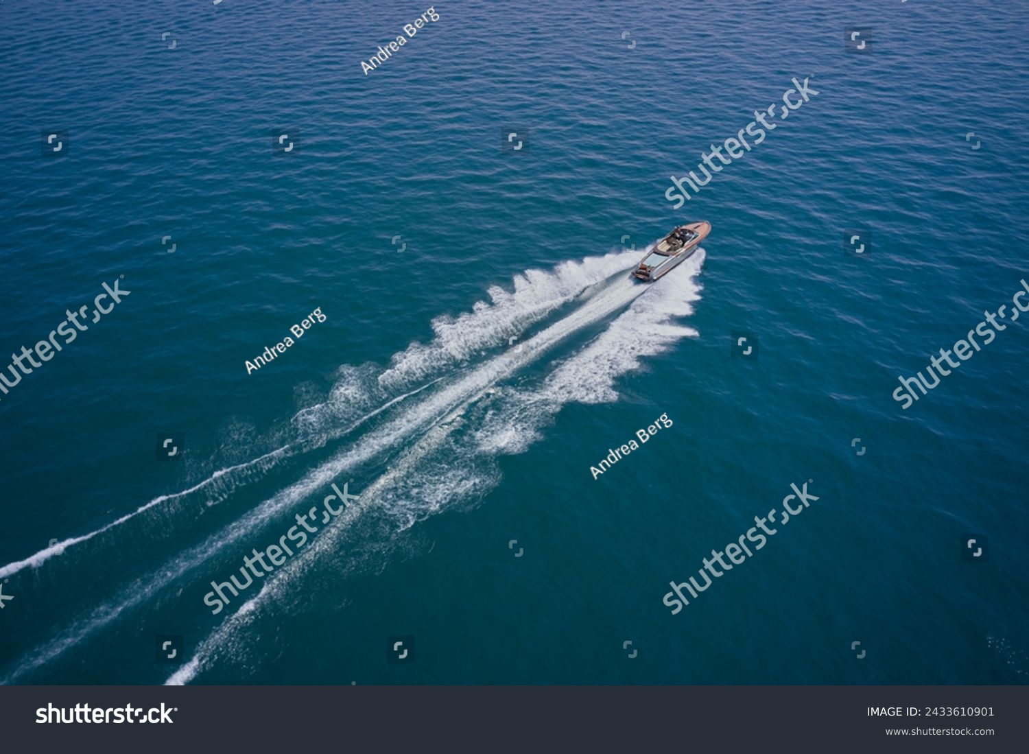 A large modern high-speed wooden luxury boat moves on blue water, top view. Expensive wooden boat, man and woman in motion on the water making a white trail looking like air. #2433610901