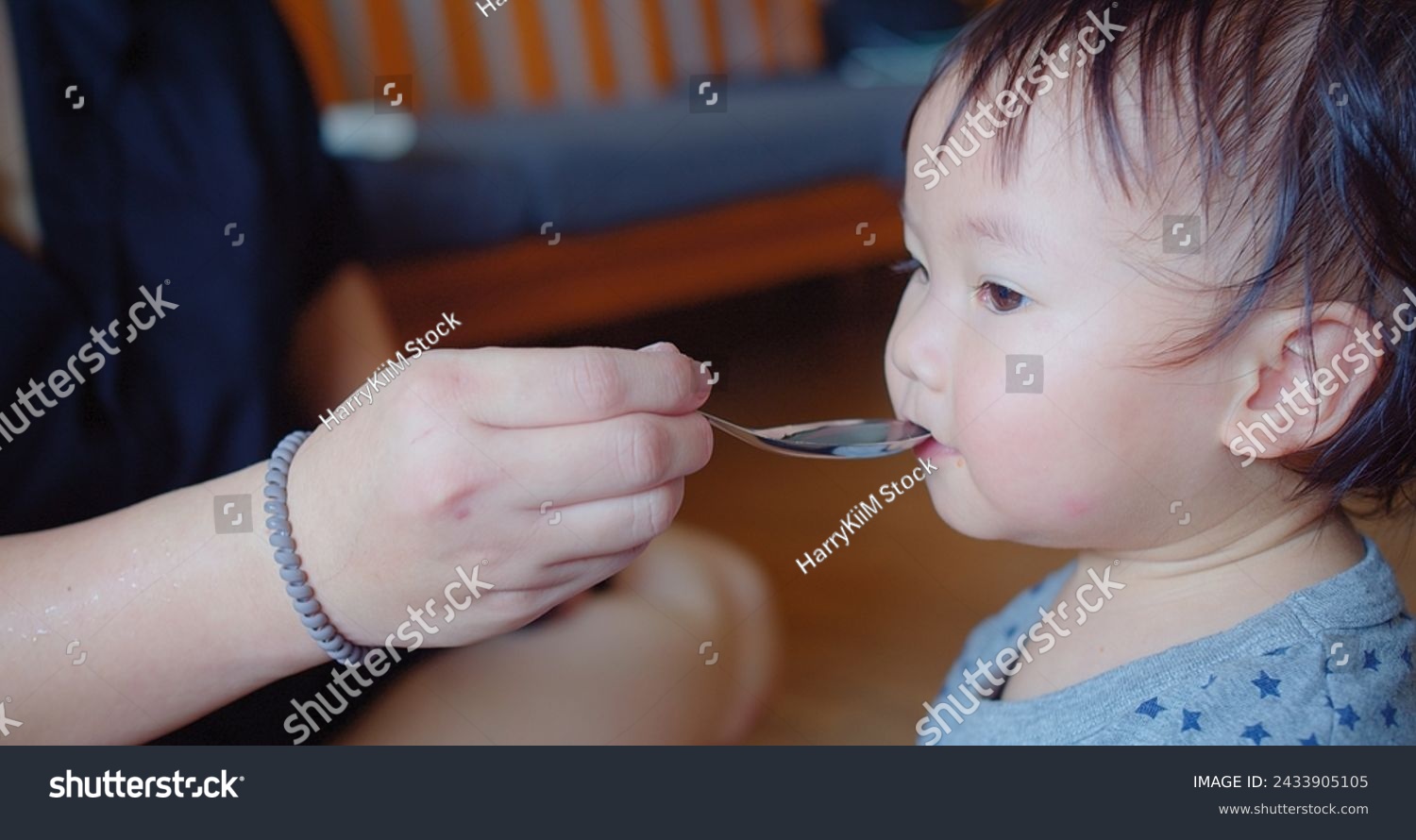 An eager toddler opens wide for a spoonful of food during a messy yet joyful feeding time at home #2433905105