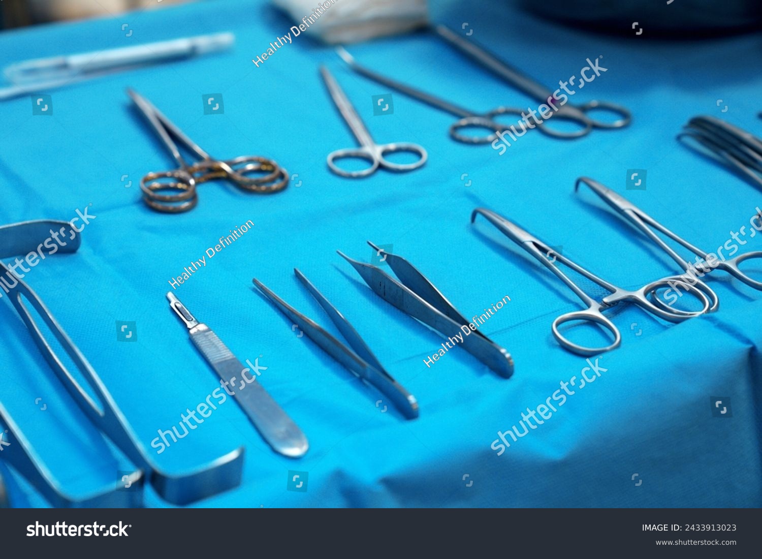 Sterile surgical instruments and tools including scalpels, scissors, forceps and tweezers arranged on a table for a surgery, Sterilized surgical instruments on the blue wrap	 #2433913023