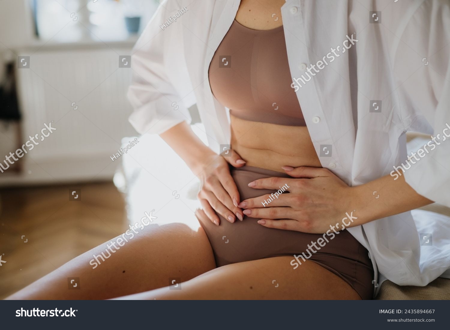 Woman at home suffering from menstrual pain, having cramps. Close up of woman holding abdomen, endometriosis, and conditions causing pain in tummy. #2435894667