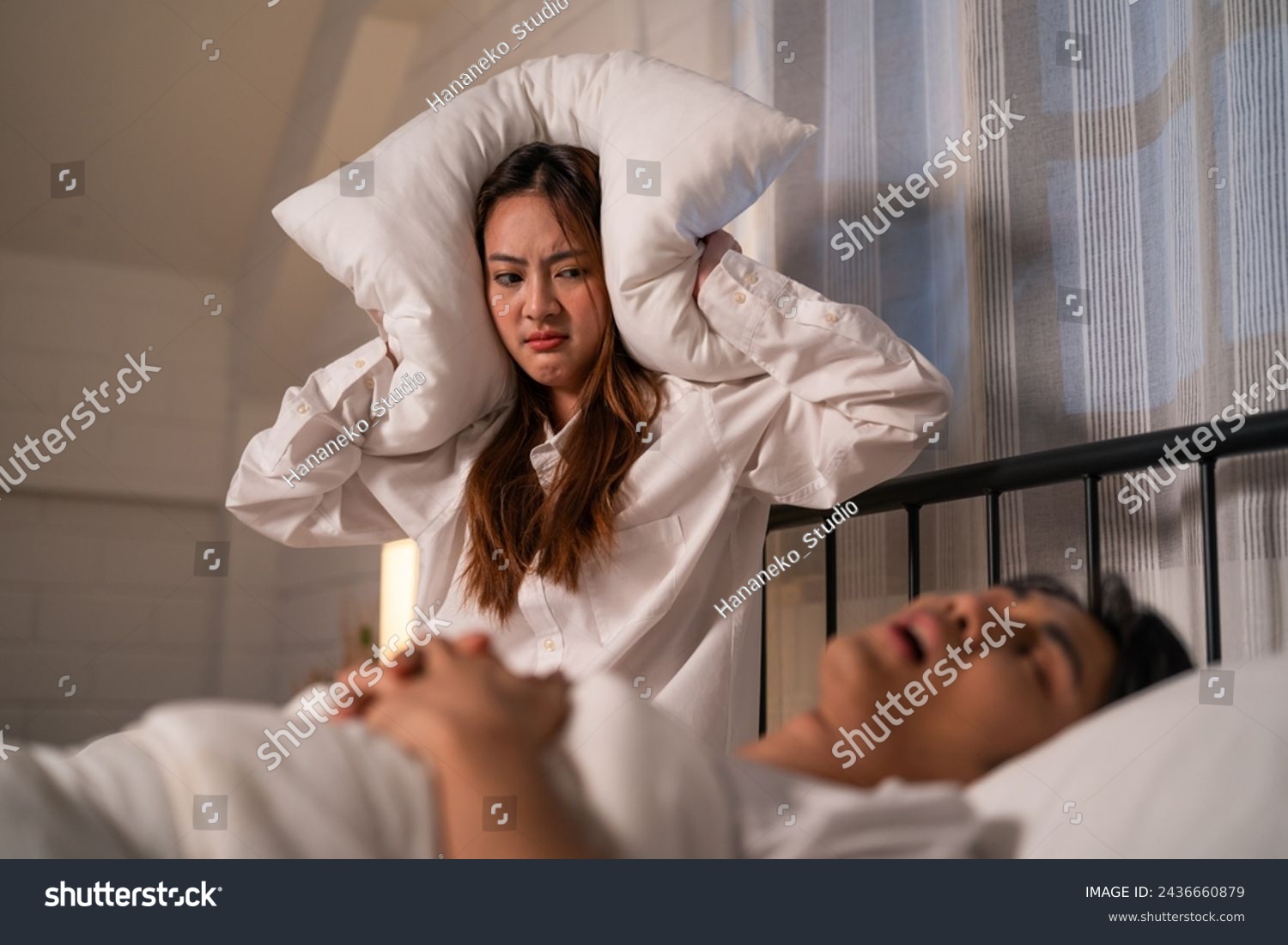 Asian woman feel frustrated from husband snoring while sleep at night. Attractive insomnia angry wife sitting on bed, cannot sleep due to noise and put cozy blanket on her ears in bedroom at home.
 #2436660879