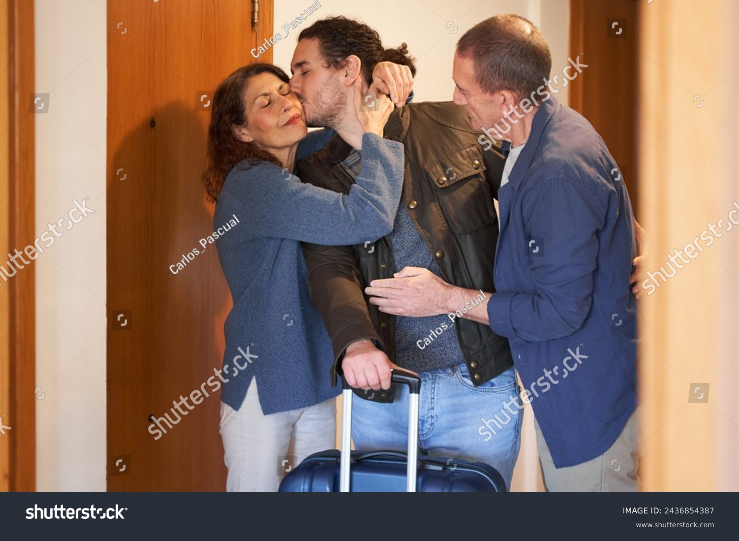 Son leaving parents concept. Son with suitcase hugging parents before moving out #2436854387