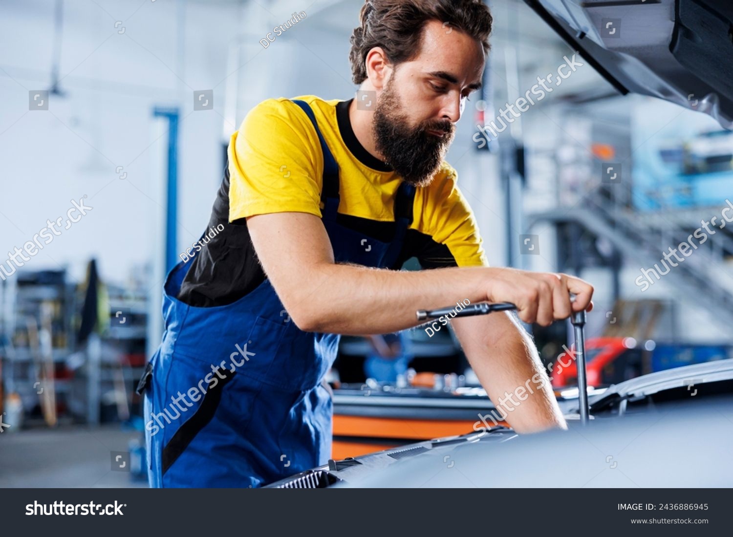 Repairman in car service uses torque wrench to tighten bolts after replacing compressor belt. Trained auto repair shop worker uses professional tools to fix customer automobile #2436886945