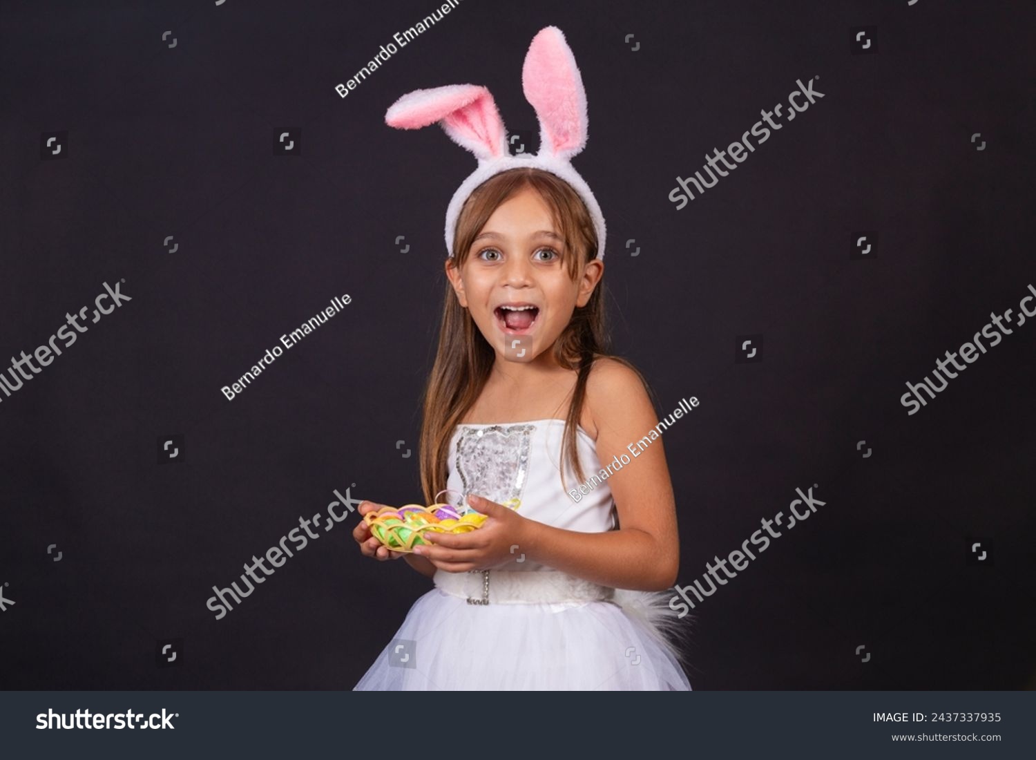 Cute little girl wearing bunny ears on Easter day. Girl holding basket with painted eggs. #2437337935
