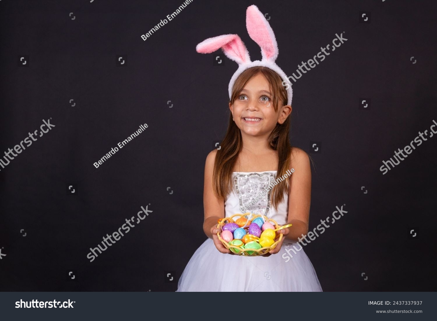 Cute little girl wearing bunny ears on Easter day. Girl holding basket with painted eggs. #2437337937
