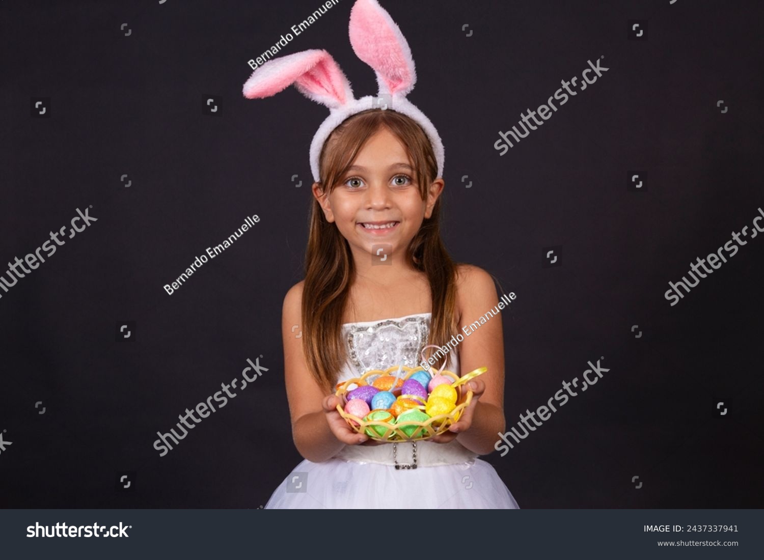 Cute little girl wearing bunny ears on Easter day. Girl holding basket with painted eggs. #2437337941