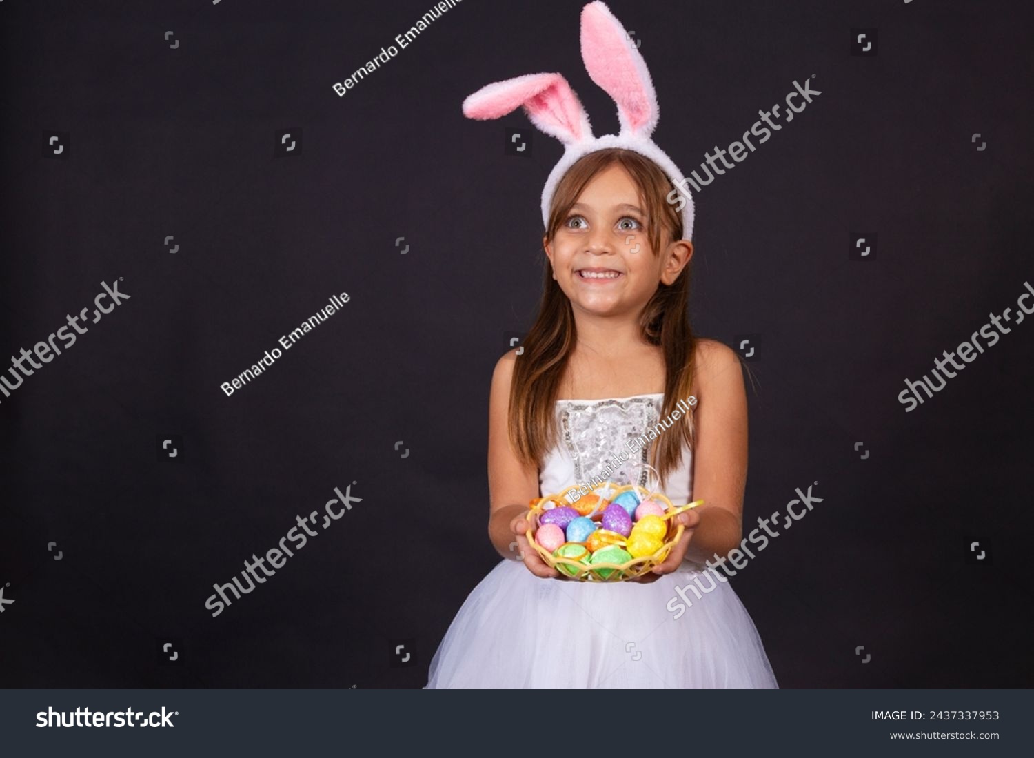 Cute little girl wearing bunny ears on Easter day. Girl holding basket with painted eggs. #2437337953