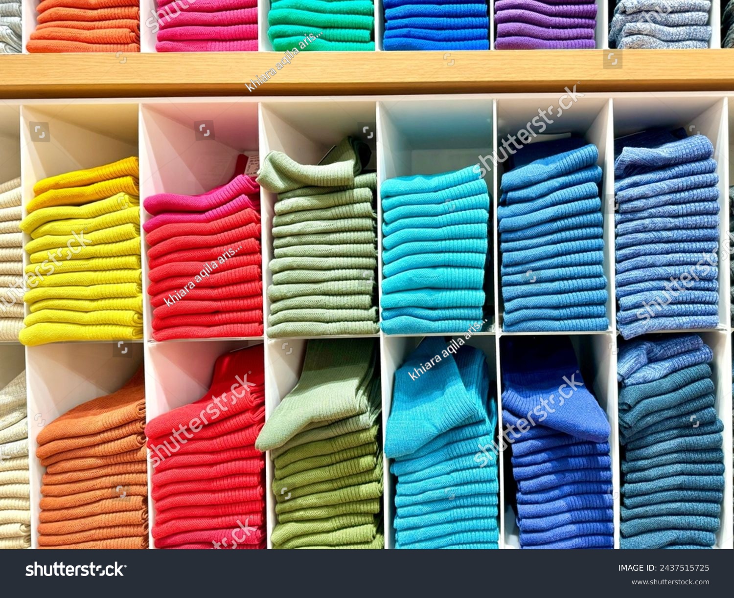 The arrangements of colors in clothes, home or shop to look attractive and tidy. Knitted clothes on shelf in a store. Neat row of clothes in assortment. #2437515725