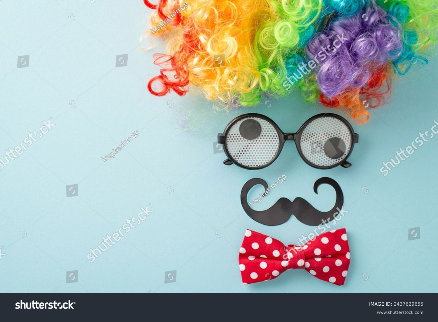 April Foolery display: top view photo with humorous goggles, buffoon's wig, neckwear, and pretend mustache, assembled to imitate a person's facial features on a pastel blue canvas, space for messaging #2437629655