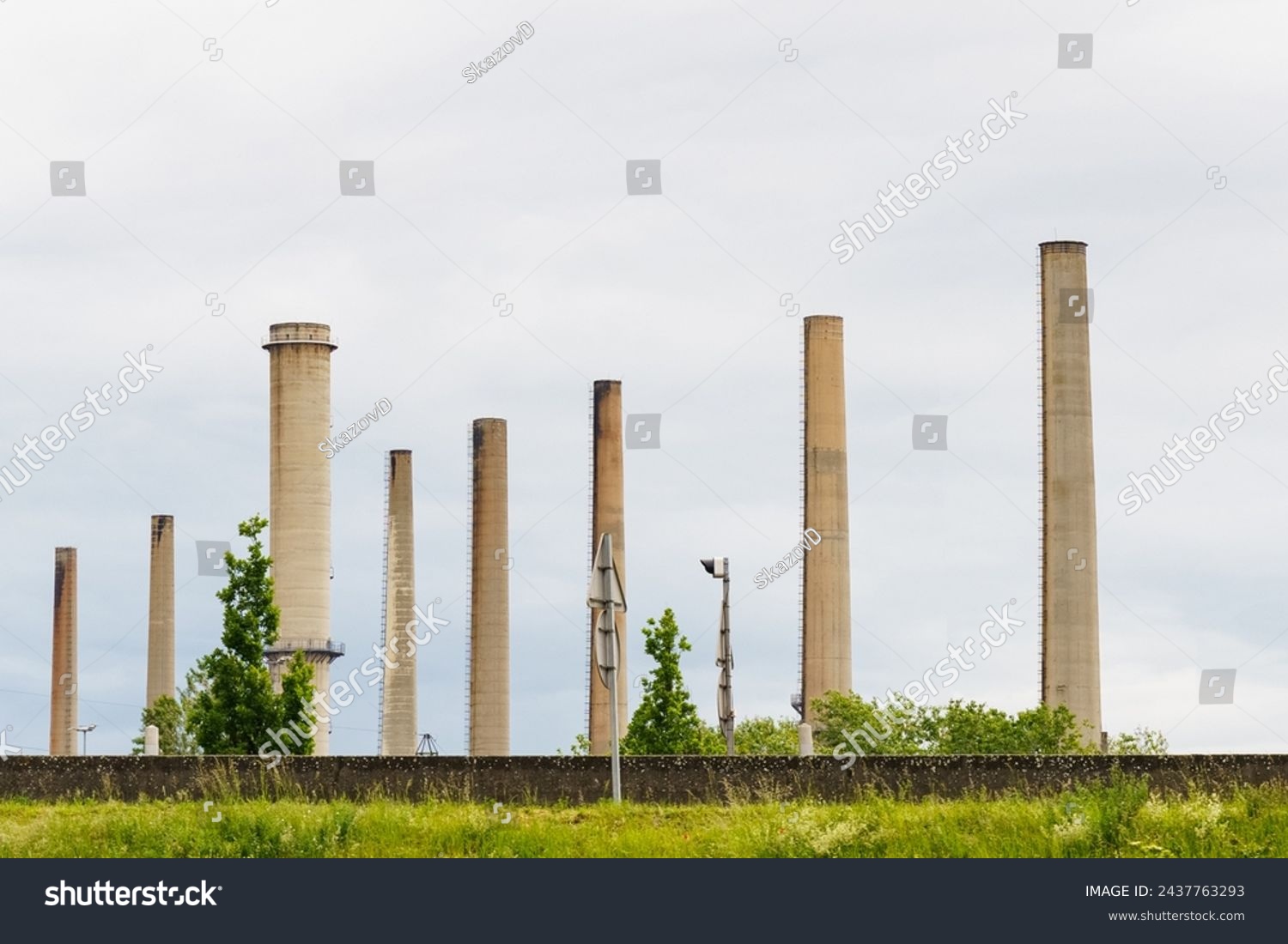A row of tall, disused industrial smokestacks stands against a cloudy sky, remnants of a bygone manufacturing era, showcased here in a quiet state of neglect. #2437763293