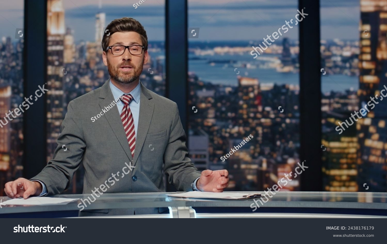 News presenter broadcasting studio. Positive bearded anchor man gesturing hand bringing up important day events. Authority announcer sharing latest evening updates delivering information at work  #2438176179