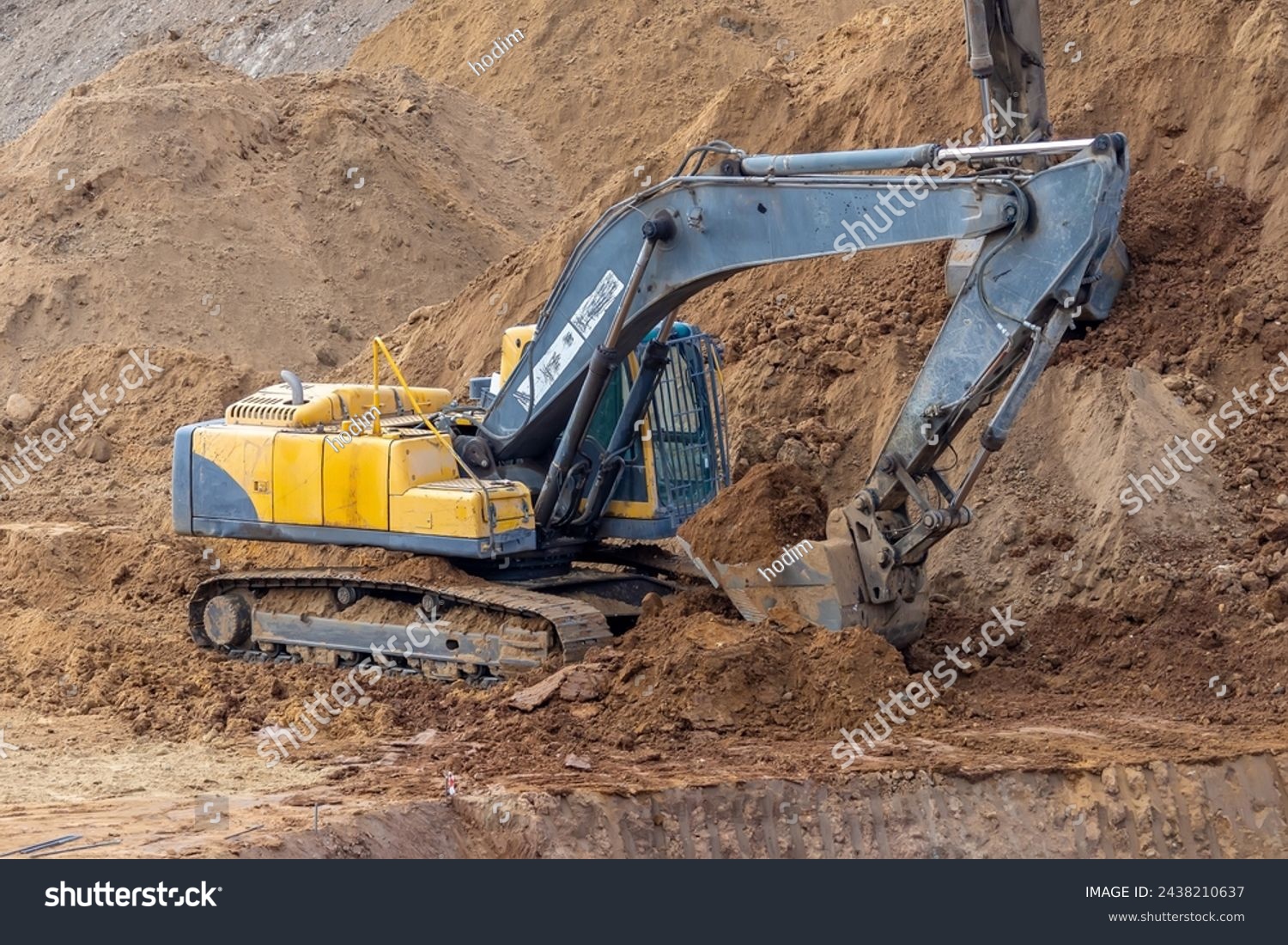 A crawler excavator is at work, the bucket is filled with soil. The machine ensures the development of land at the construction site. The excavator shows signs of dirt and wear, indicating heavy use #2438210637
