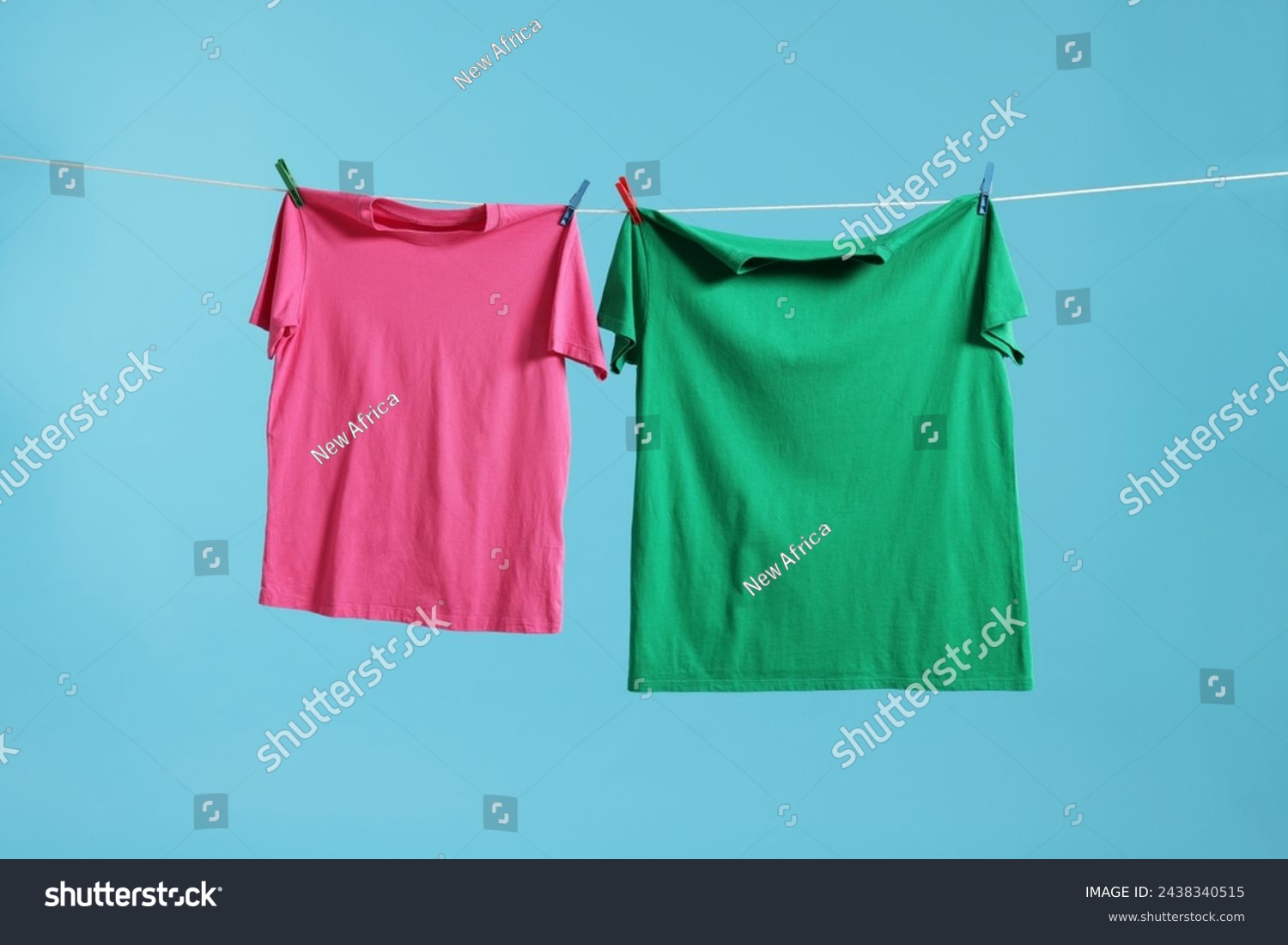 Two colorful t-shirts drying on washing line against light blue background #2438340515
