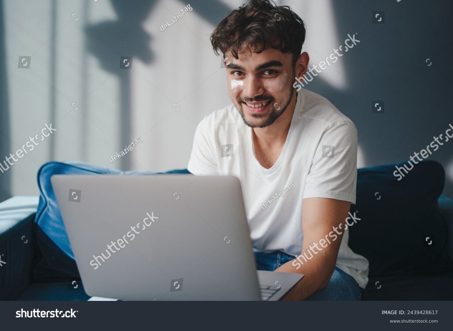 Portrait of young smiling man holding pc on lap sitting on the sofa in living room, typing on keyboard. Cheerful guy browsing internet, surfing web. People and #2439428617