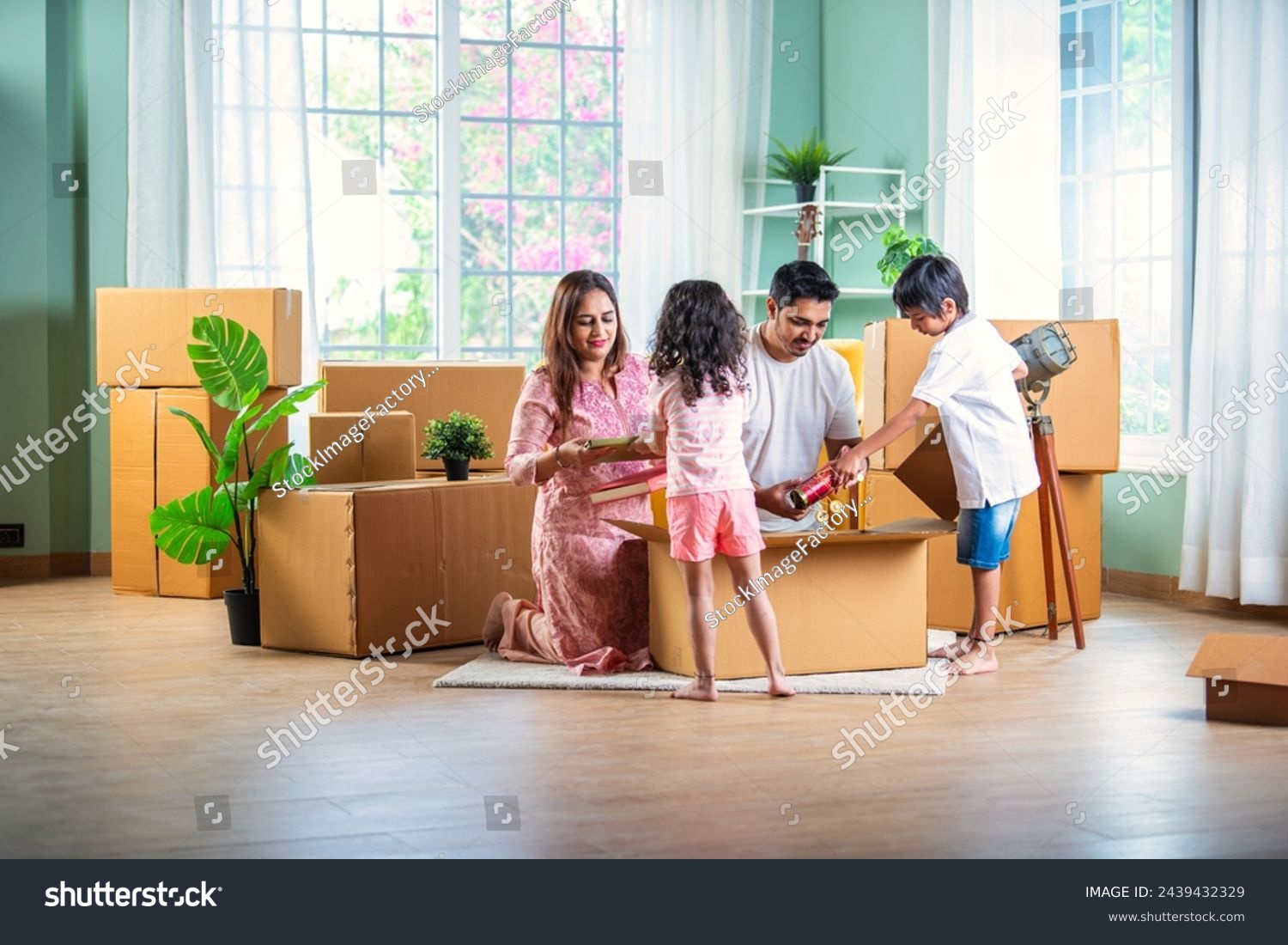 House move concept. Happy Indian young family sitting on the floor in new home #2439432329
