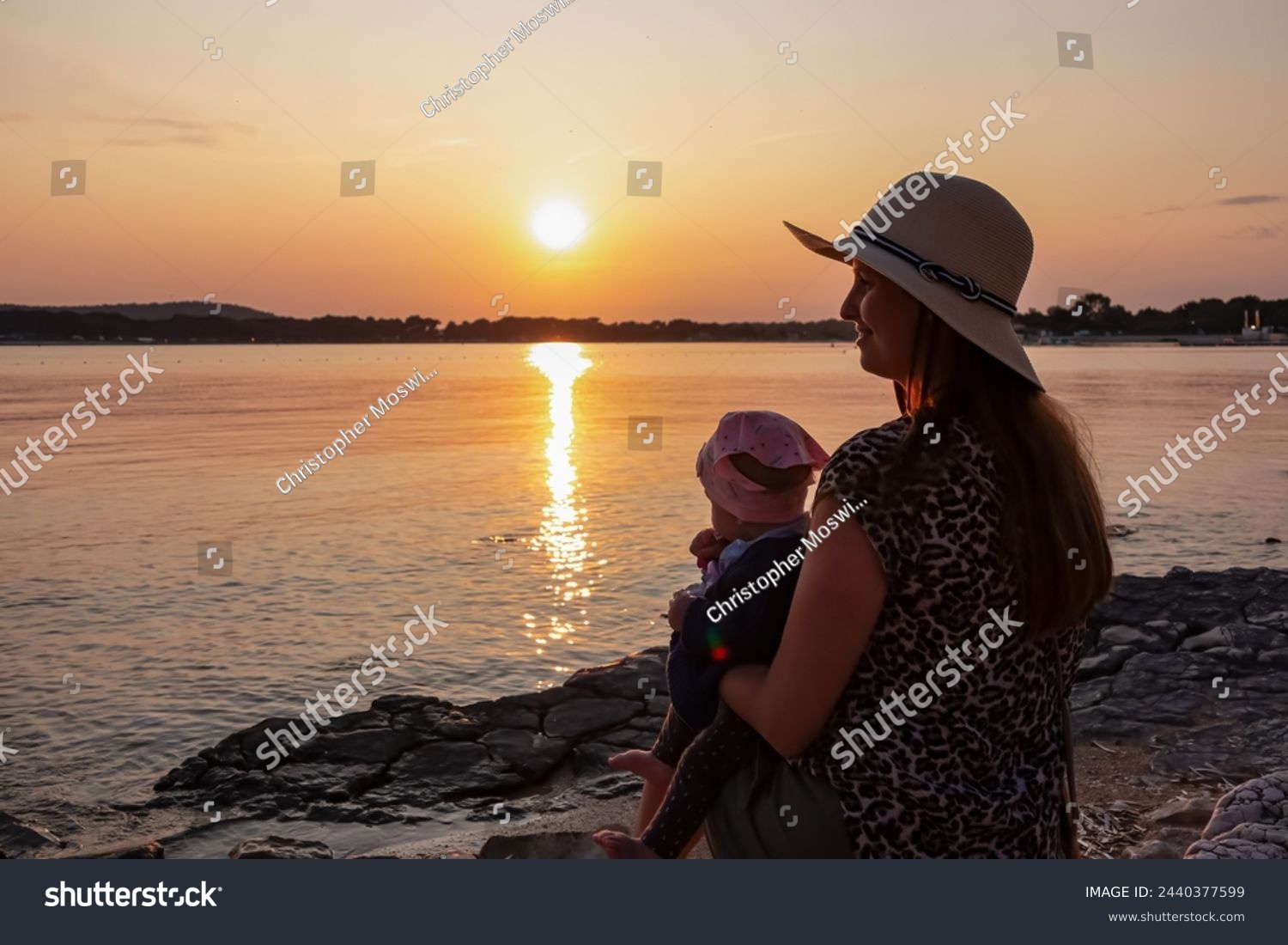 Loving mother holding small toddler enjoying romantic sunset in Medulin, Istria, Croatia, Europe. Coastline of Kvarner Gulf in Adriatic Mediterranean Sea. Dreamlike atmosphere. Family vacation concept #2440377599