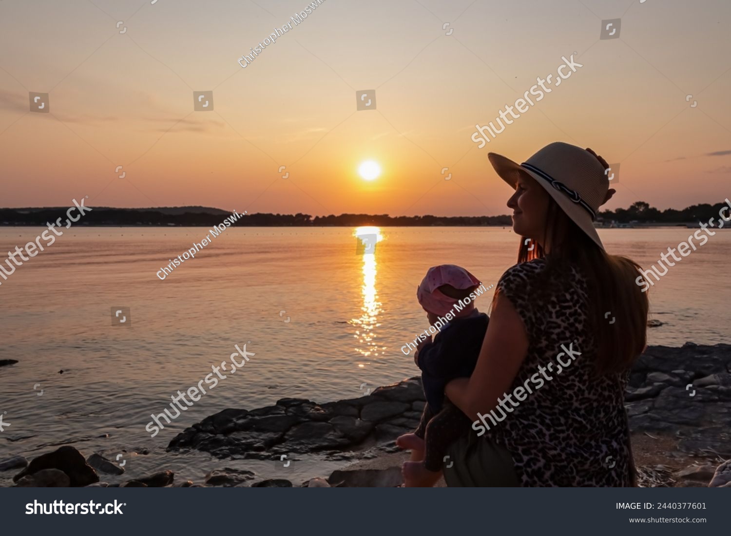 Loving mother holding small toddler enjoying romantic sunset in Medulin, Istria, Croatia, Europe. Coastline of Kvarner Gulf in Adriatic Mediterranean Sea. Dreamlike atmosphere. Family vacation concept #2440377601