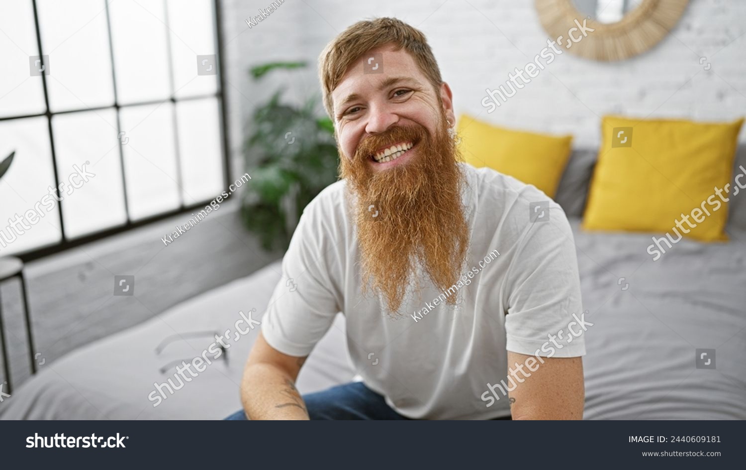 Wake up to a charming morning with a young, happy redhead man, sitting comfortably in bed, smiling confidently in his cozy bedroom, enjoying a relaxing moment of home comfort. #2440609181