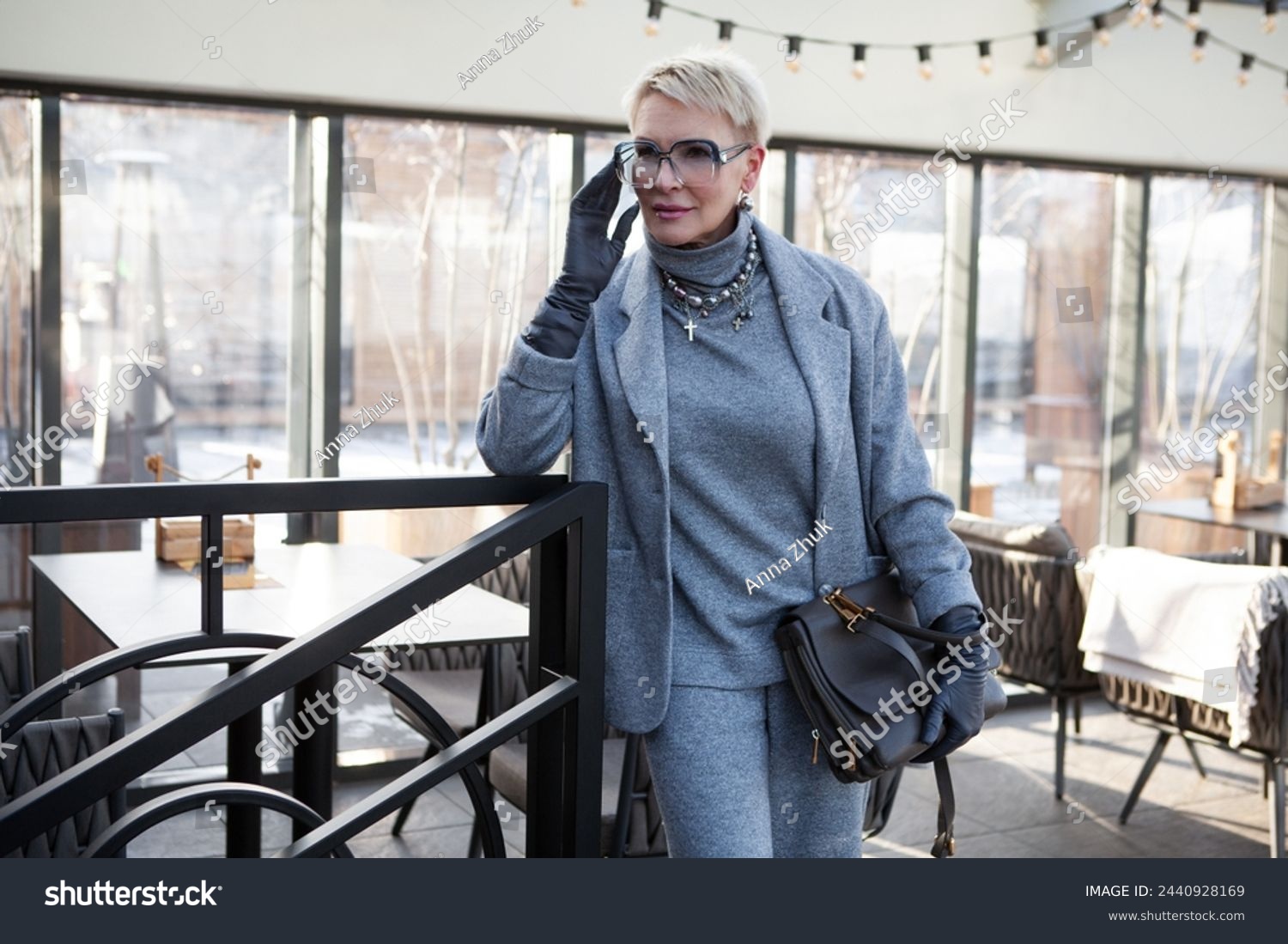 Attractive and stylish mature woman in grey pant suit with jacket and turtleneck, accessorized with handbag. The perfect look for successful women over 50. #2440928169