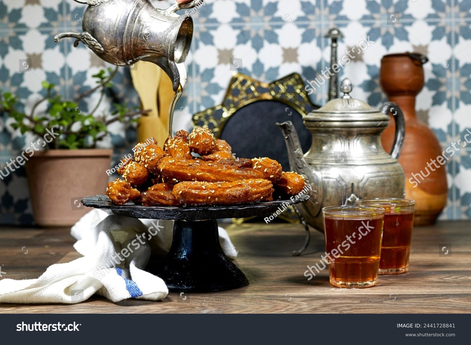 woman pouring a honey sirup on algeria oriental Balah el sham dessert fritters named zlabiat al banan in algerian language with arabic tea #2441728841