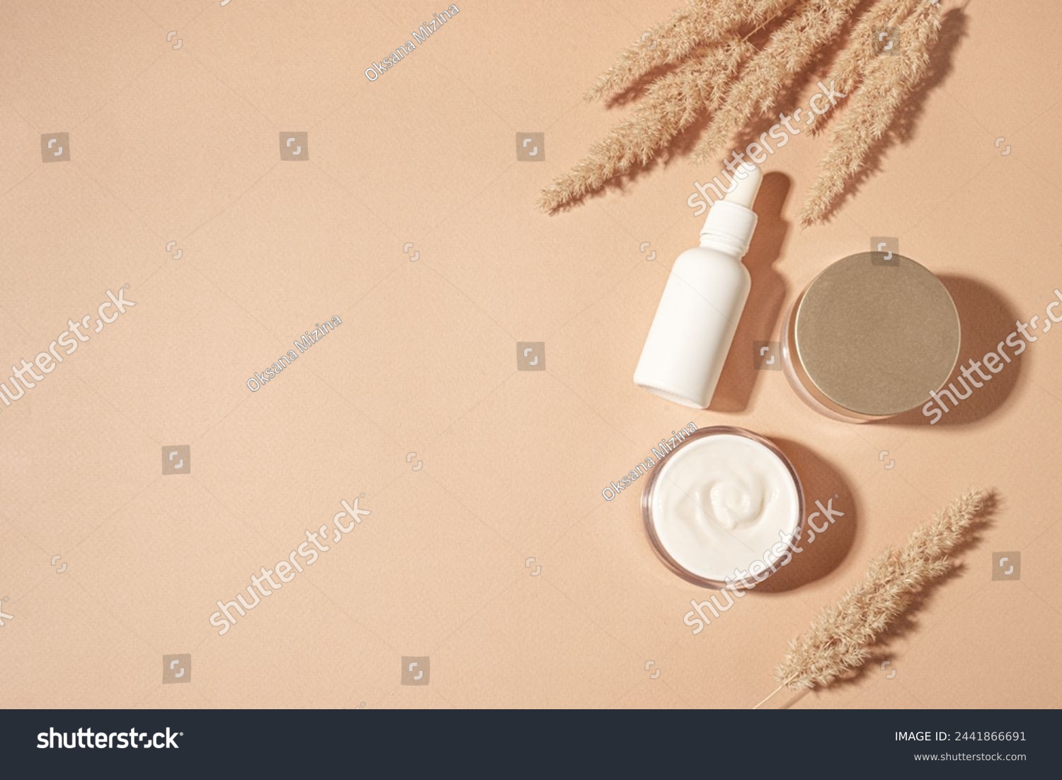 Cosmetic serum and beauty cream products with dry reeds or pampas grass on neutral beige background, trendy flat lay with hard shadows. Facial anti age natural skin care, copy space. #2441866691