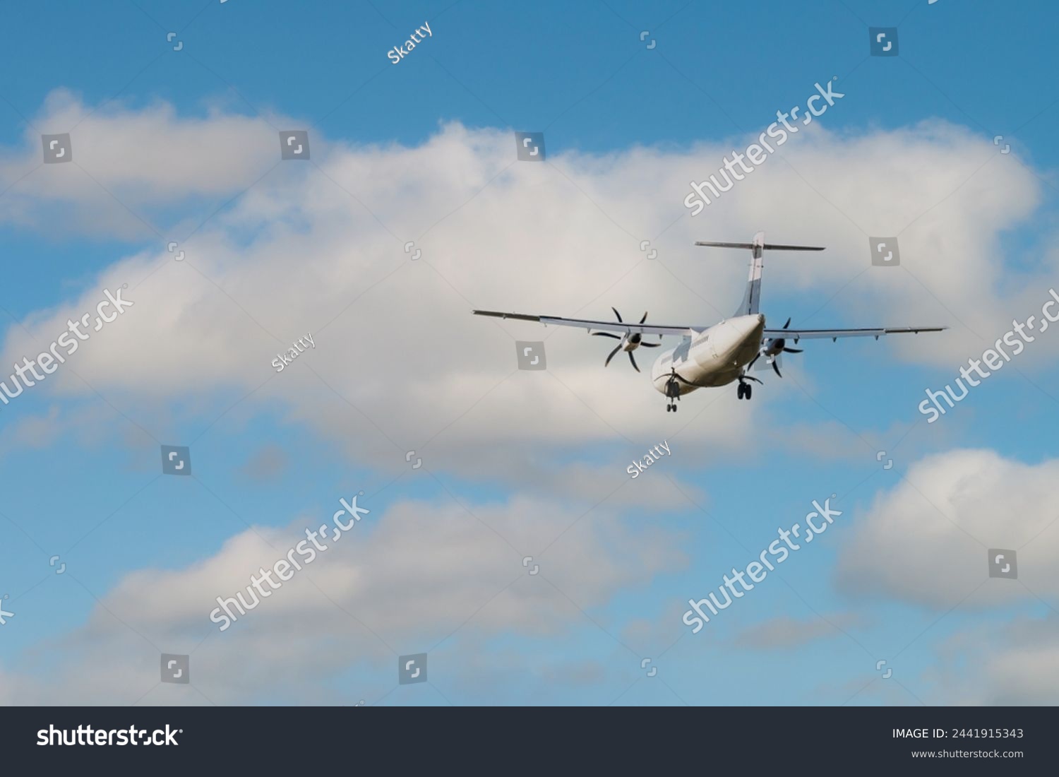 Rear view of an ATR 72 airplane among the clouds. Twin-engine turboprop short-haul regional passenger aircraft. Landing airplane. #2441915343