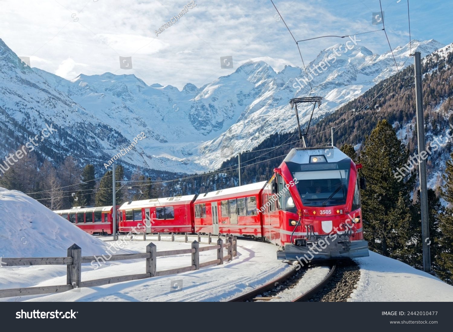 A Bernina Express travels thru Montebello Curve on a sunny winter day, with Morteratsch Glacier lying below Piz Bernina and snowy mountains in background in Pontresina, Graubünden, Switzerland, Europe #2442010477