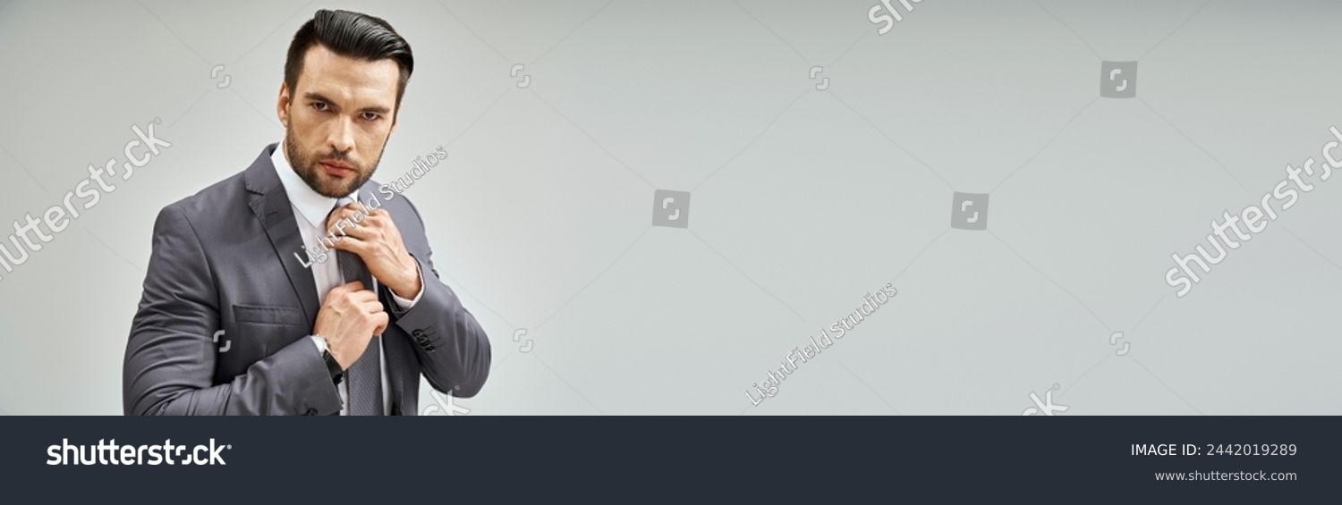 thoughtful man in formal wear adjusting tie on grey background, corporate fashion banner #2442019289