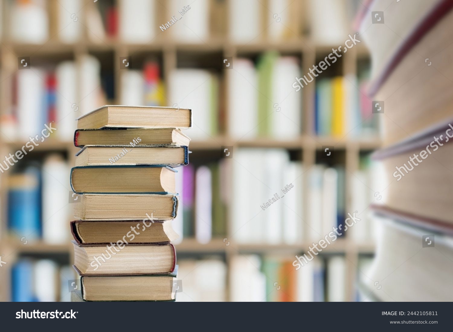 A stack of textbooks against a background of bookshelves in a library. #2442105811