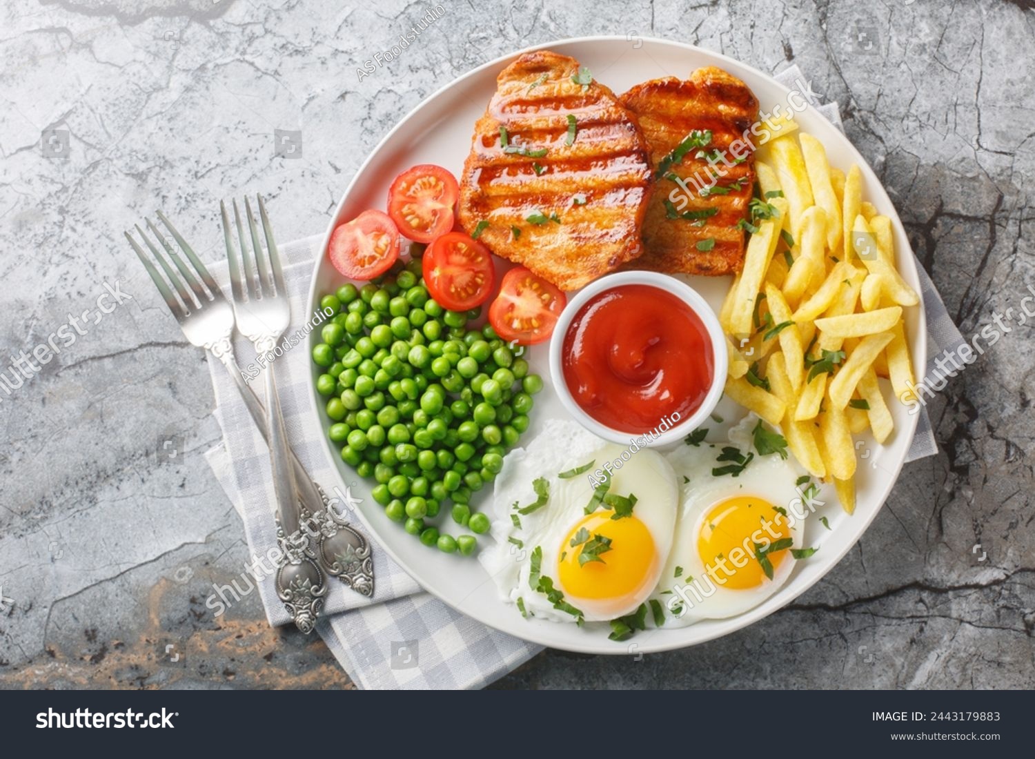 Tender grilled steak served with crisp golden French fries, fied eggs, green pea and fresh tomato closeup on the plate on the table. Horizontal top view from above
 #2443179883