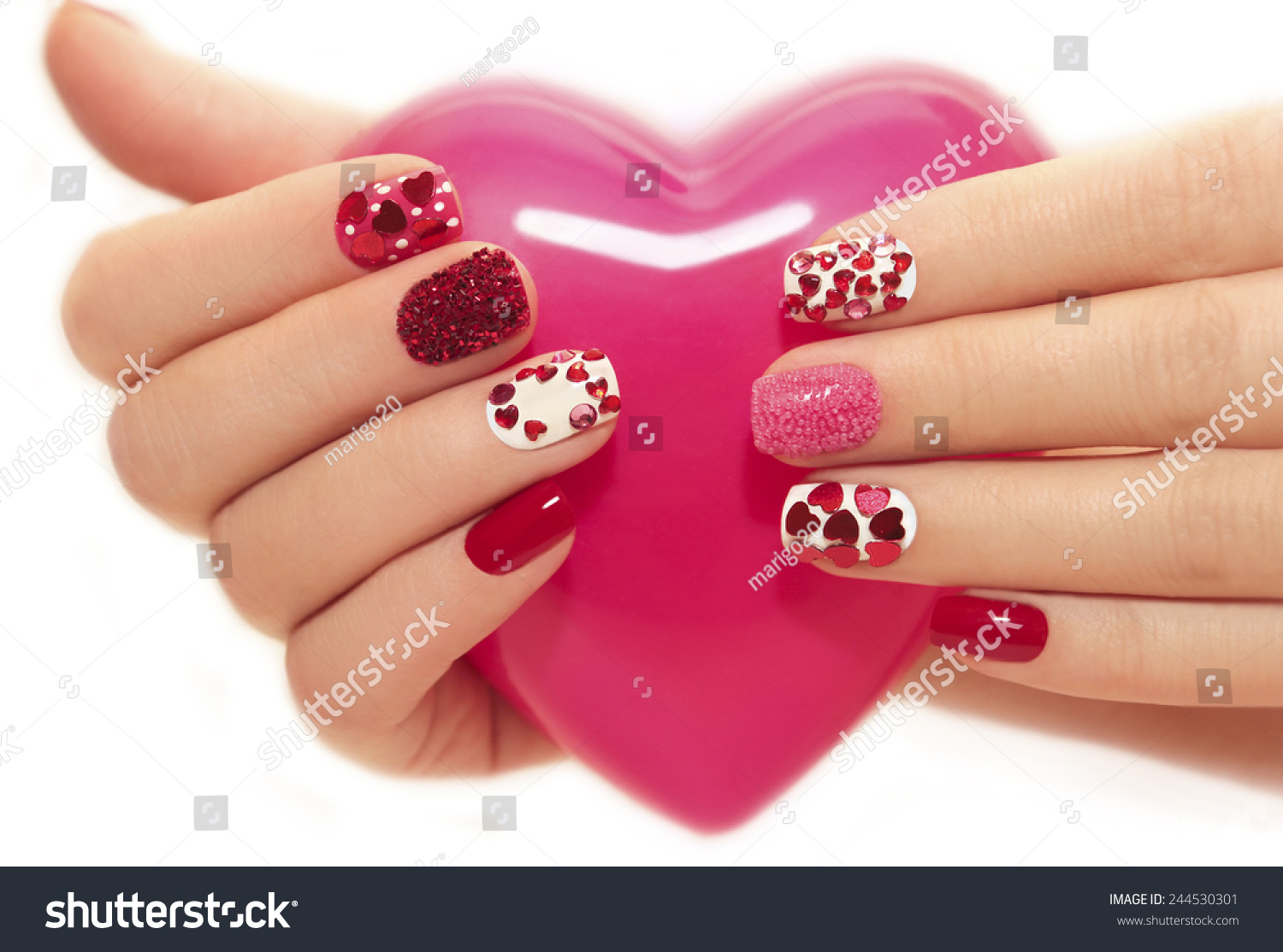 Manicure with rhinestones in the shape of hearts and pink balls on white and red nail Polish on a white background. #244530301