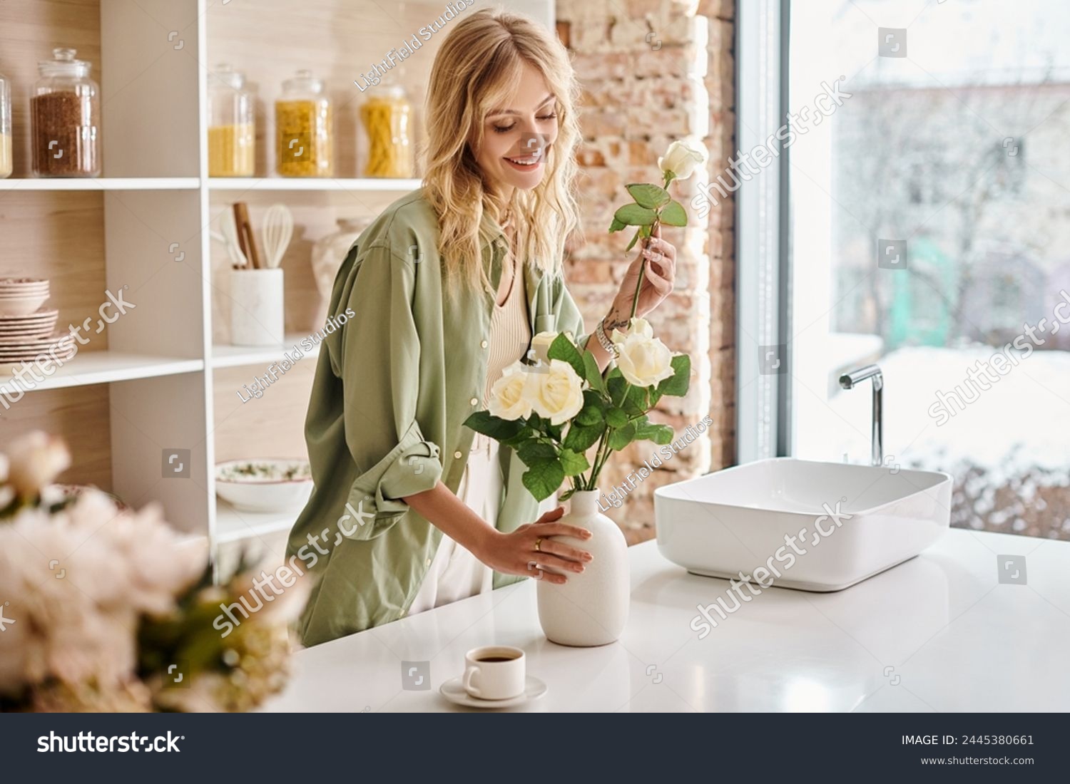 Woman in kitchen arranging colorful flowers in a vase at home. #2445380661
