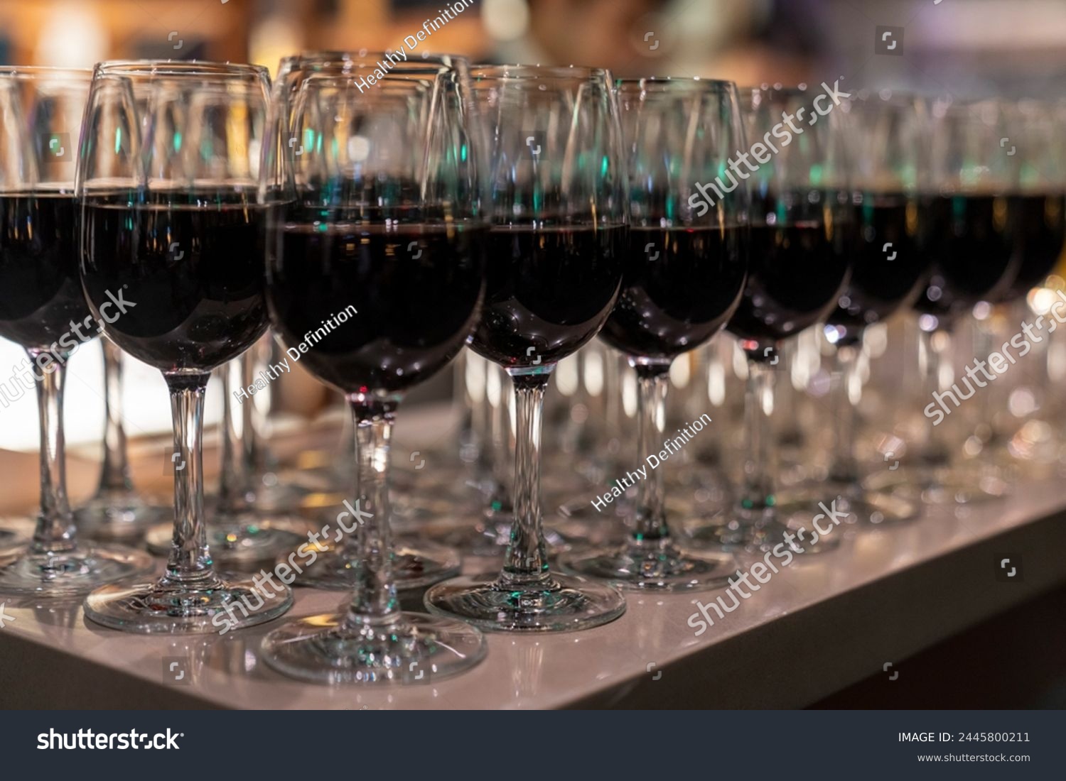 Wine glasses filled with red wine arranged and presented on a table top for self-service by party guests. Shallow depth-of-field image. A glass of red wine is on the table. Glasses of wine.  #2445800211