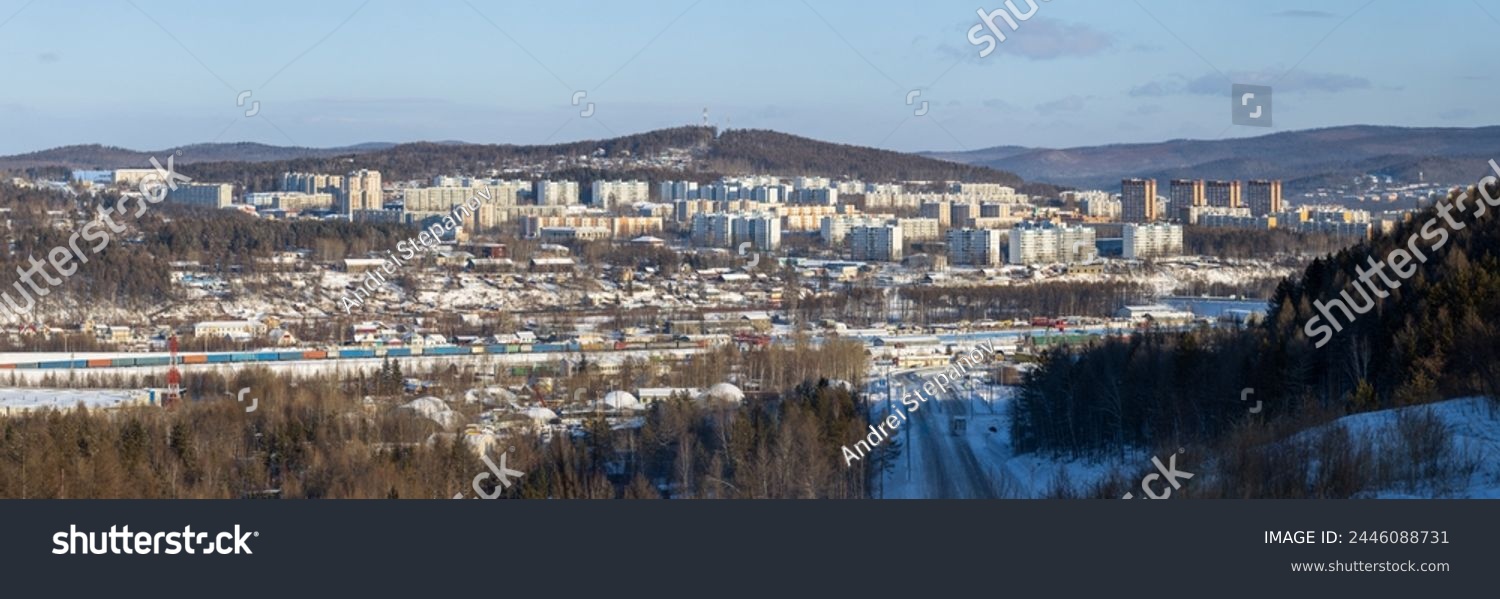 Tynda city, Amur region, Siberia, Russia. Winter panoramic city landscape. In the distance are residential buildings and hills. In the middle ground there is a railway. In the foreground is a road. #2446088731