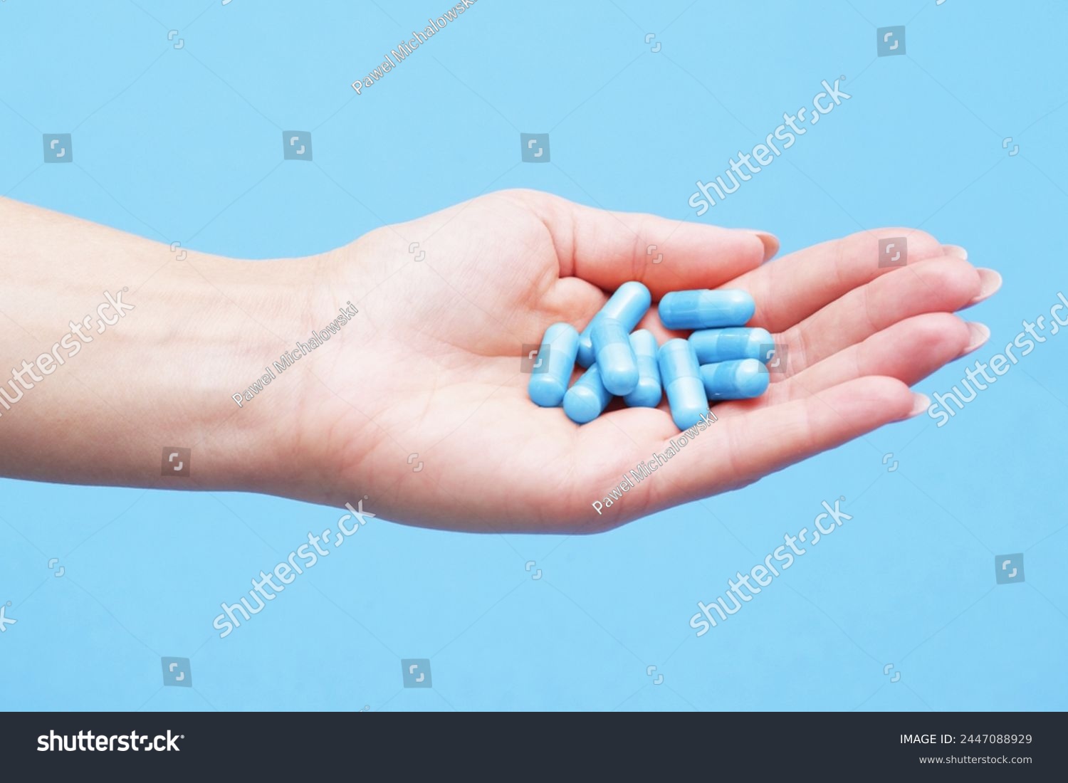 Medicine background. Blue pills isolated on blue. Pile of capsules. Tablets background. Vibrant vivid color drugs. Antibiotics background. Holding blue pills. Drugs on hand. Diet supplementation. #2447088929