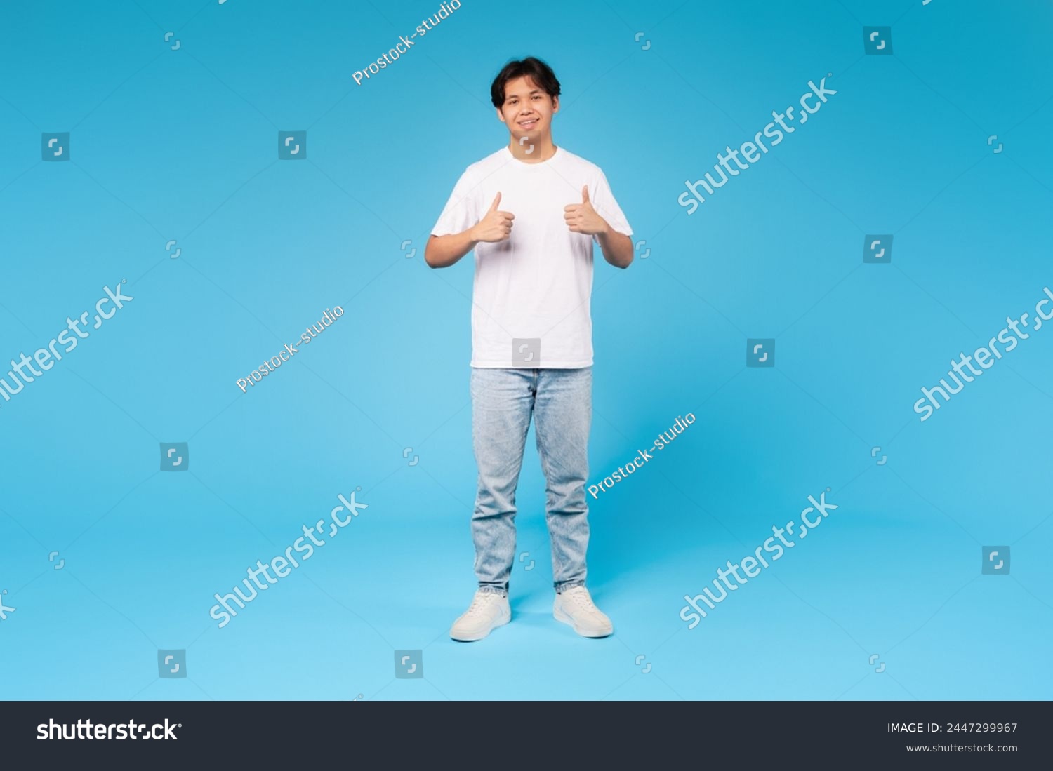 Full body portrait of a young asian guy giving two thumbs up, expressing approval and confidence on blue background #2447299967
