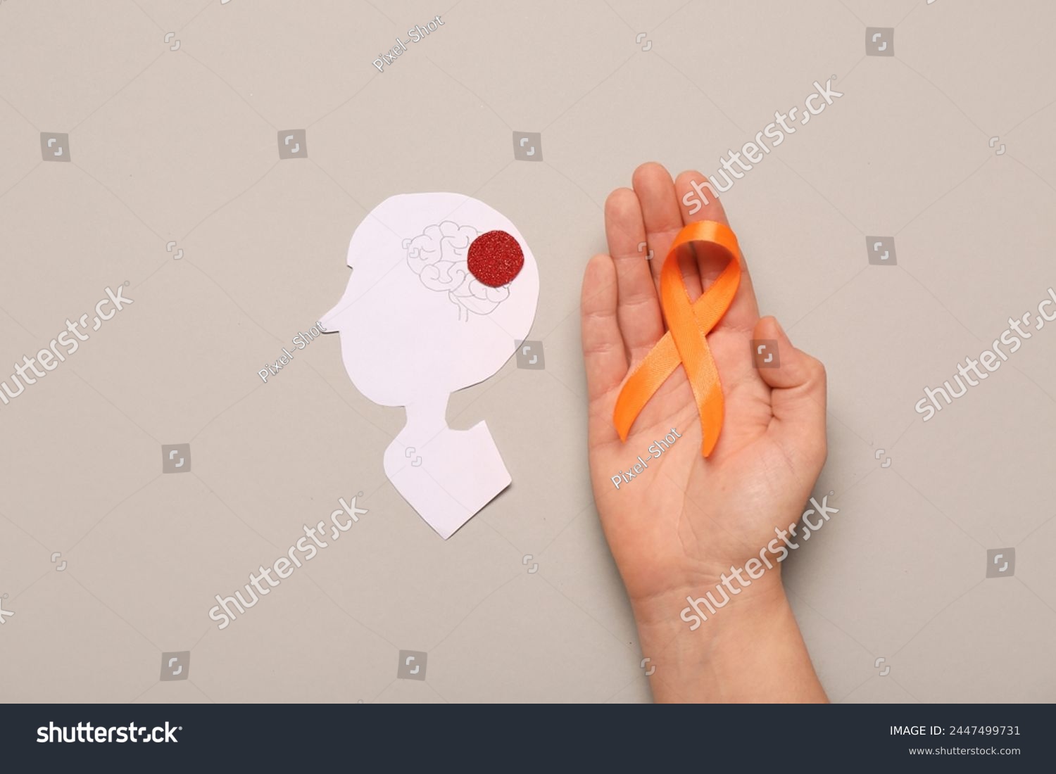 Female hand with orange ribbon and paper human head on grey background. Multiple Sclerosis Awareness Month #2447499731