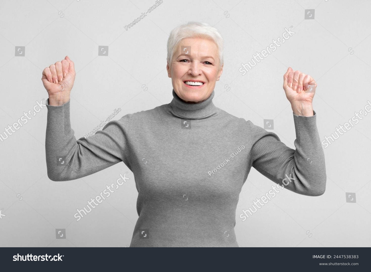 Cheerful senior european woman throws her fists up in a victory pose, ideal image for s3niorlife promotions #2447538383