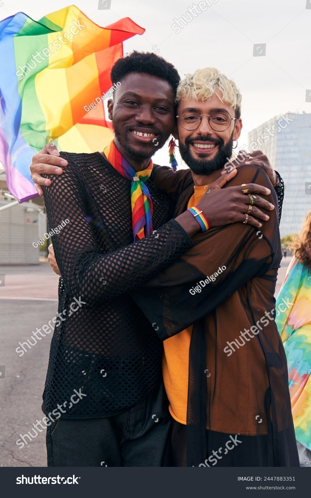 Cheerful portrait of male gay couple hugging while looking at camera smiling. Two men at pride parade celebrating the LGBTQIA month. Vertical photo with copy space. #2447883351