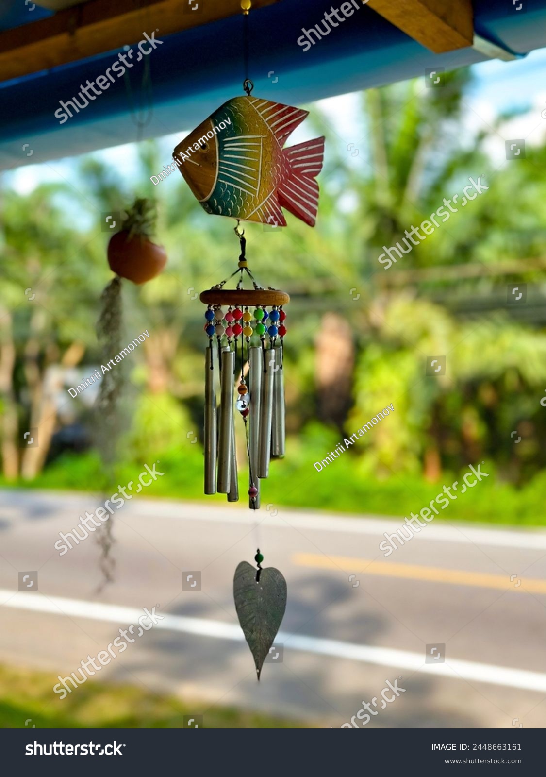 A hand-painted fish wind chime with metal tubes and beads hanging outdoors, a whimsical addition to garden decor #2448663161