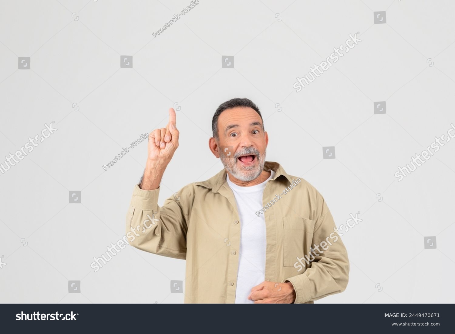 An old man shows excitement, pointing up enthusiastically, isolated on a neutral background, copy space #2449470671