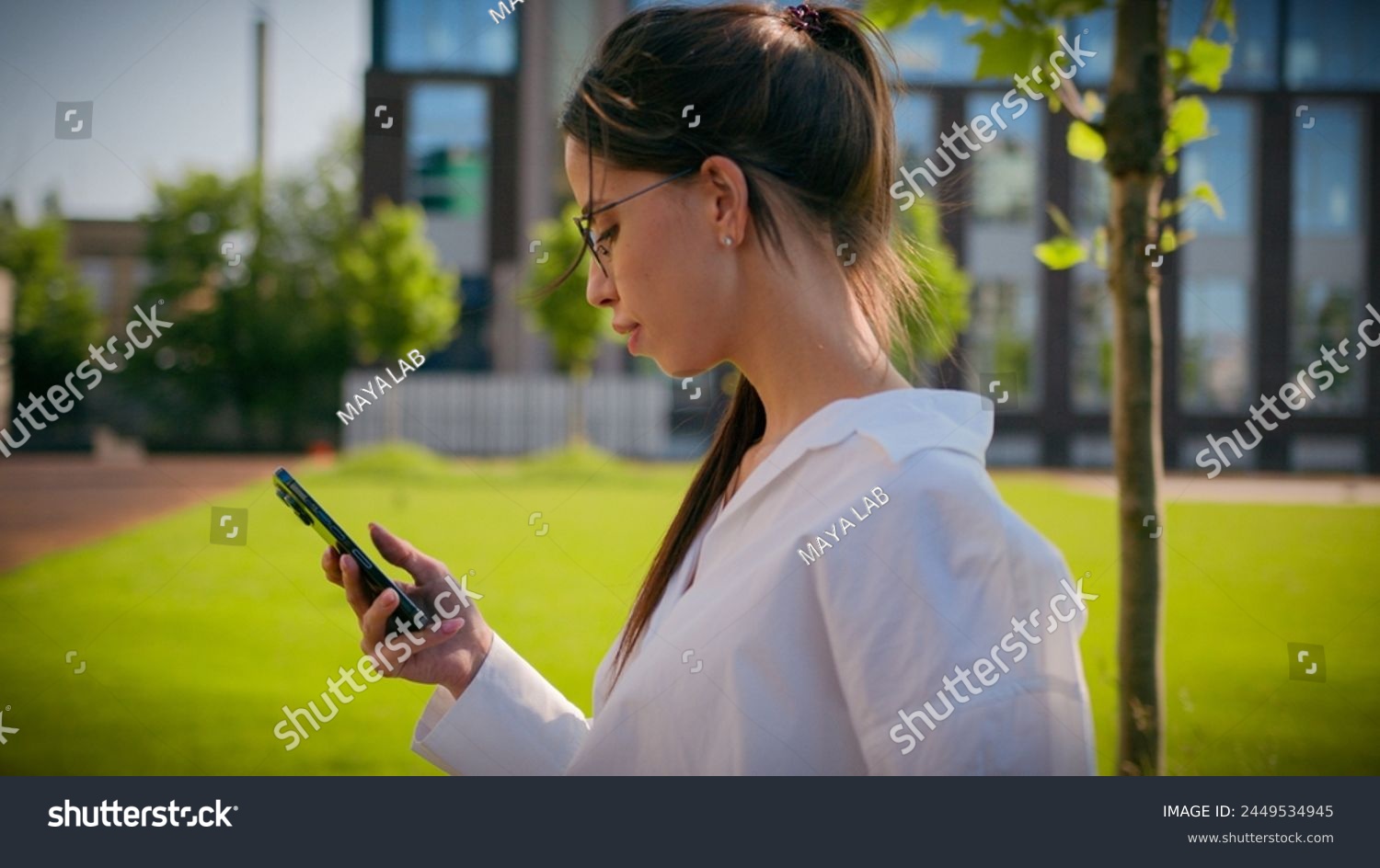 Caucasian woman businesswoman student business lady girl walk on street with green lawn using mobile phone check email browsing social network make order online store on smartphone outdoors side view #2449534945