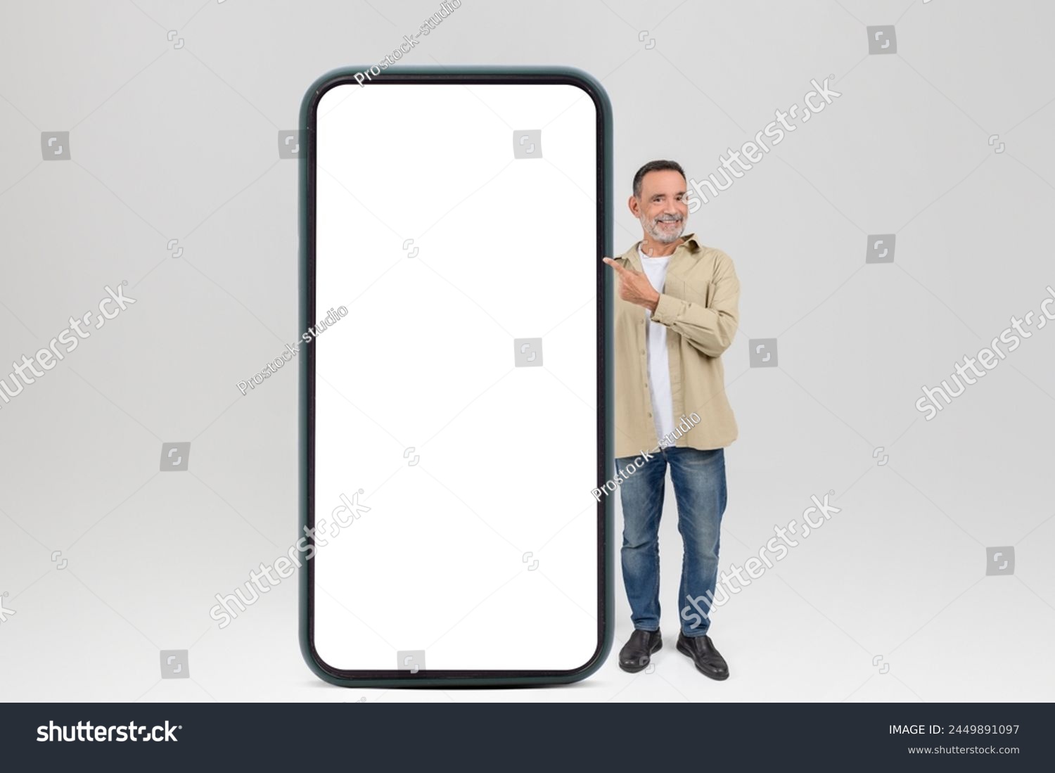 Cheerful elderly man gestures towards a blank large smartphone screen, isolated on white background, mockup, copy space #2449891097