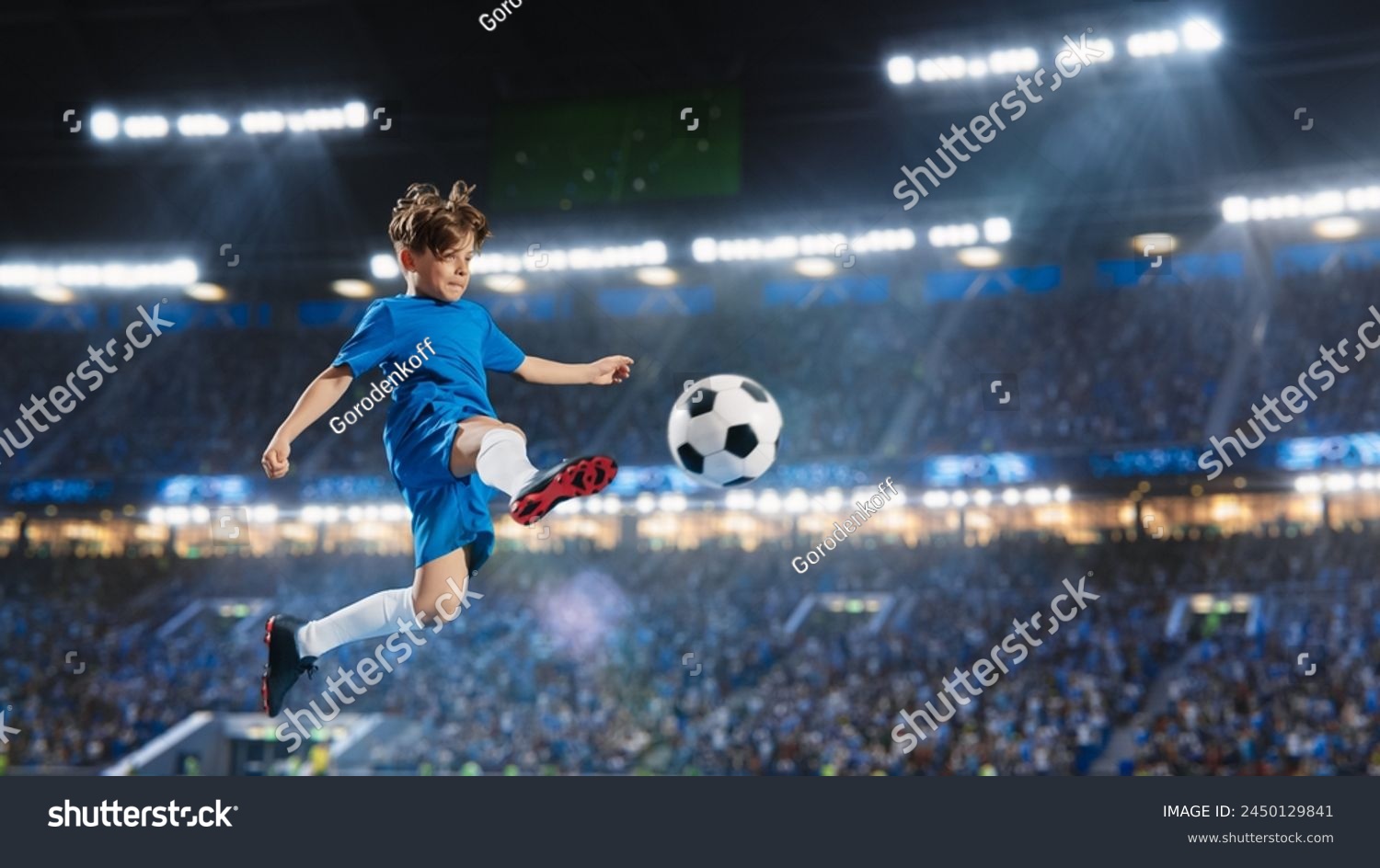 Aesthetic Shot Of Athletic Child Soccer Football Player Jumping And Kicking Ball Mid-Air On Stadium WIth Crowd Cheering. Young Boy Scoring a Winning Goal on Junior World Championship Tournament Match. #2450129841