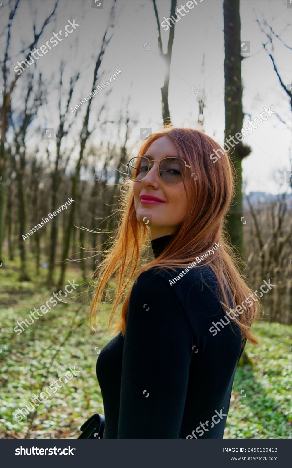 A person with obscured face stands amidst a serene forest, the sunlight filtering through bare trees creates a peaceful atmosphere, highlighting the individual’s red hair.  #2450160413